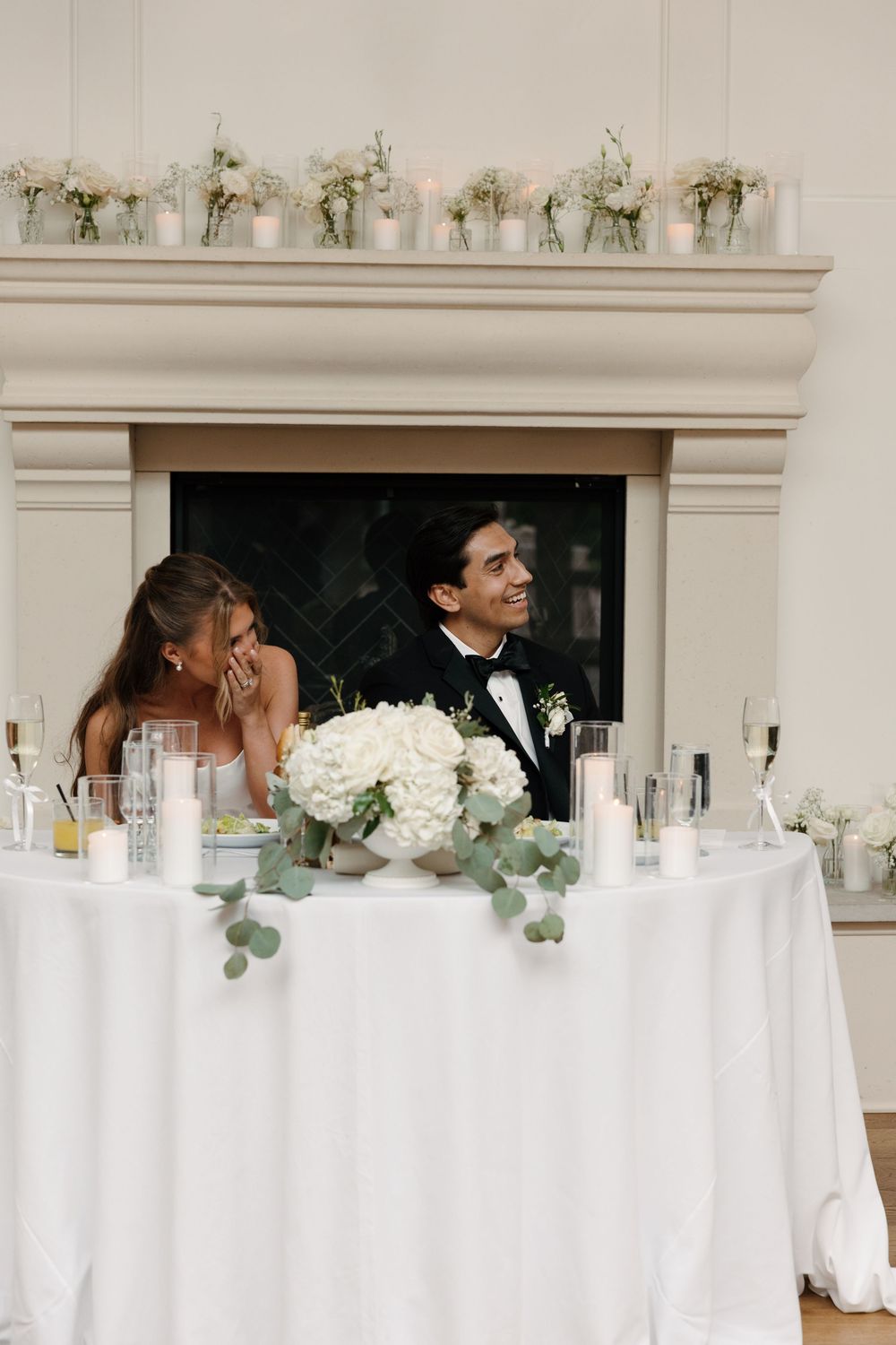 Bride and groom smiling at sweetheart table with white hydrangea centerpiece and candles at elegant wedding reception.