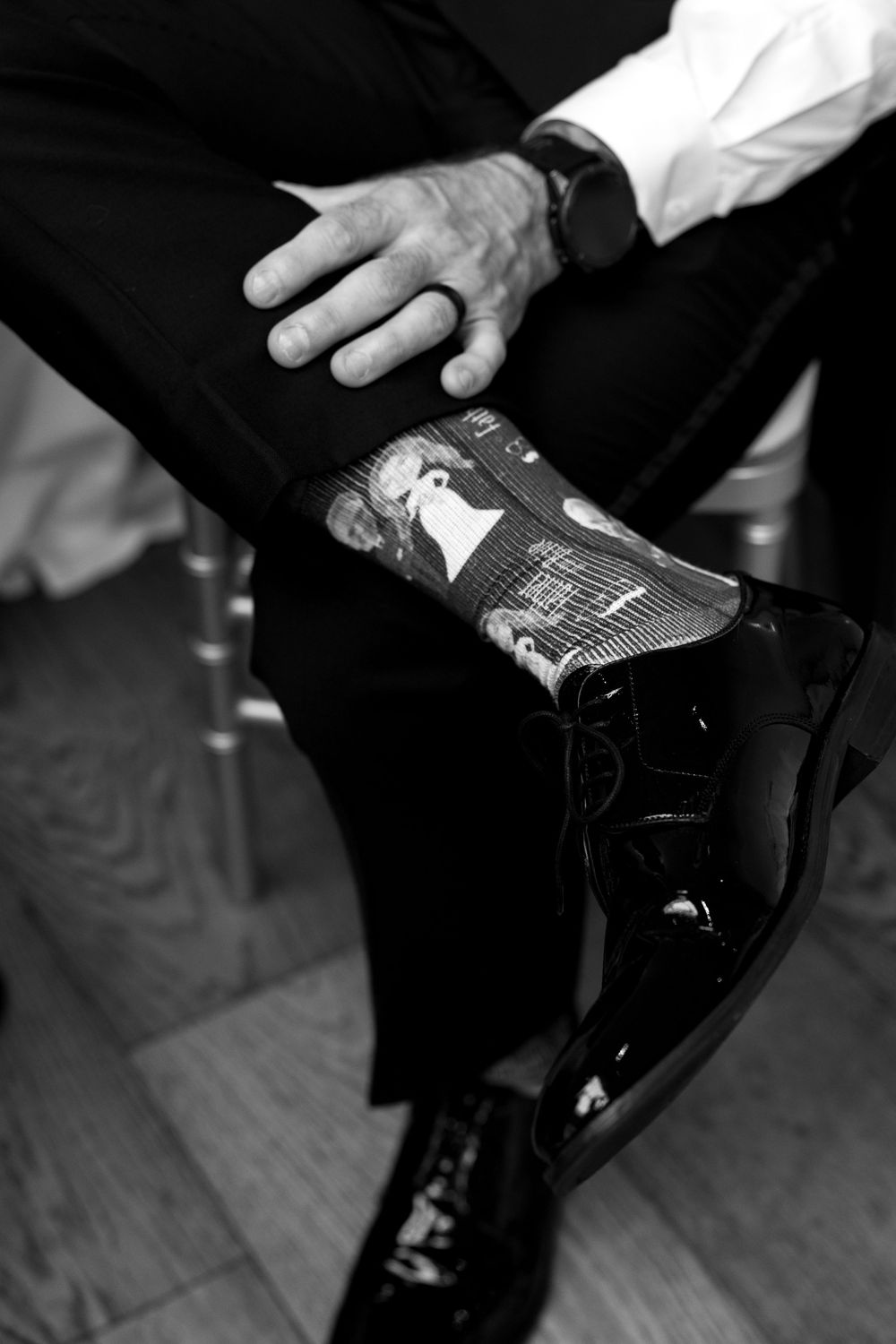 Black and white photo of groom showing custom wedding photo socks with dress shoes and suit pants.
