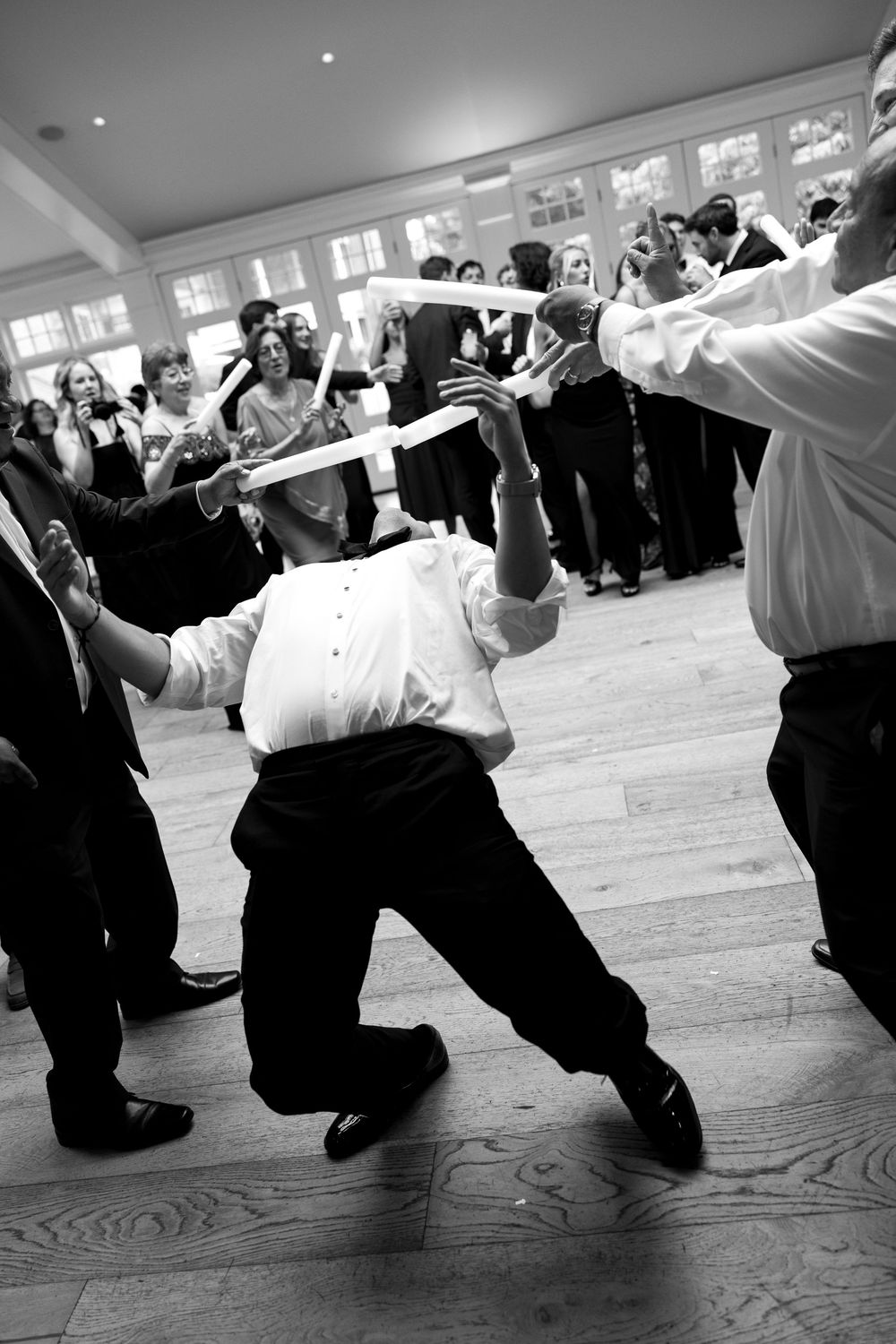Guests doing the limbo dance at a wedding reception in a elegant ballroom, black and white photo.