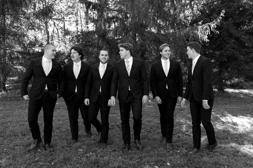 A group of people wearing black suits and formal attire walk together outdoors in a candid photo series.