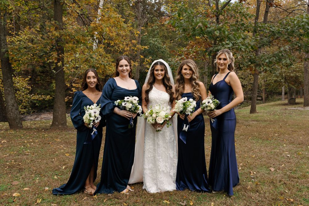 Wedding party in navy blue dresses and white bouquets poses together outdoors during autumn.