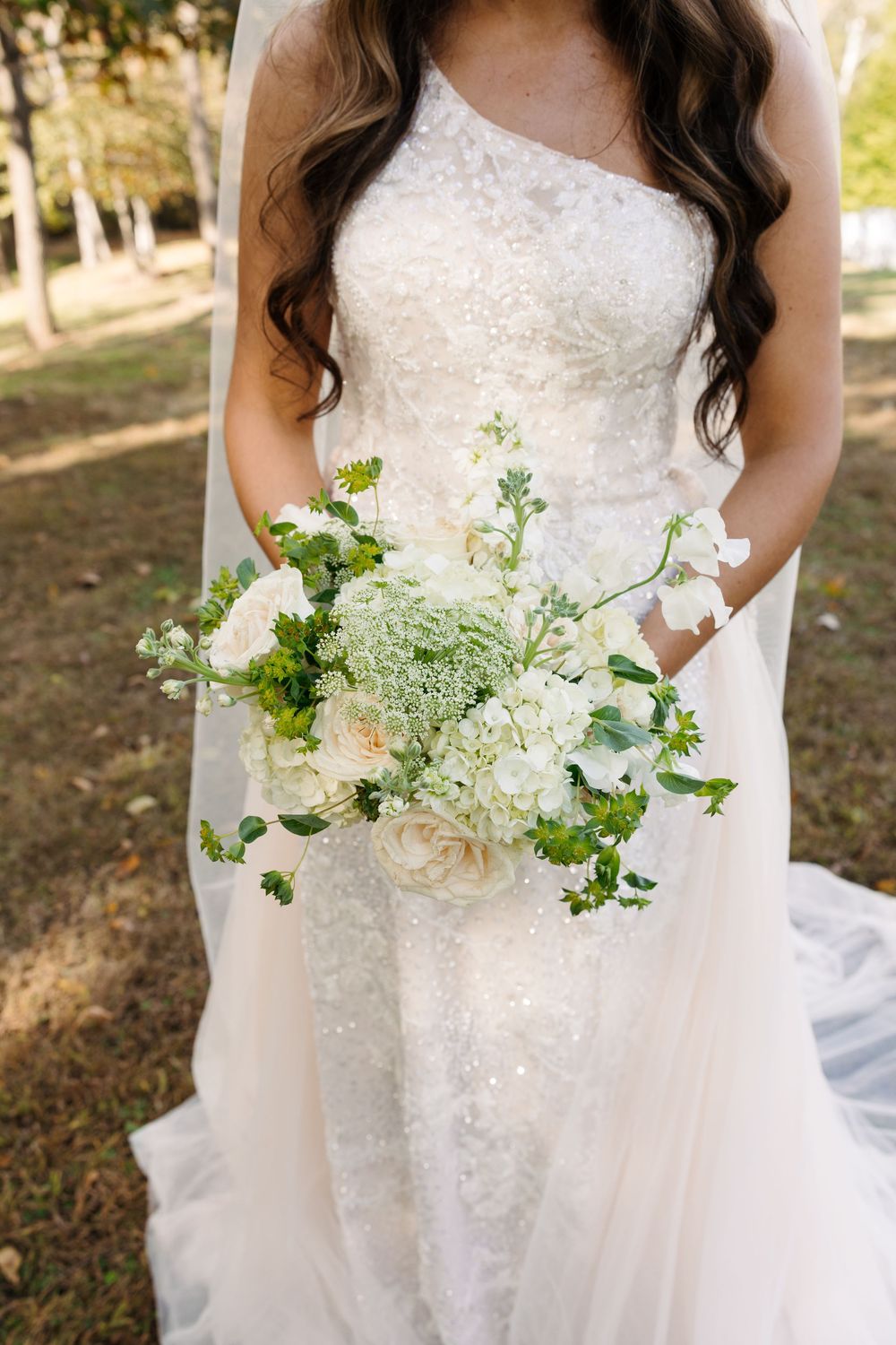 Close-up of an elegant white bridal bouquet with delicate white flowers and greenery against a wedding dress.