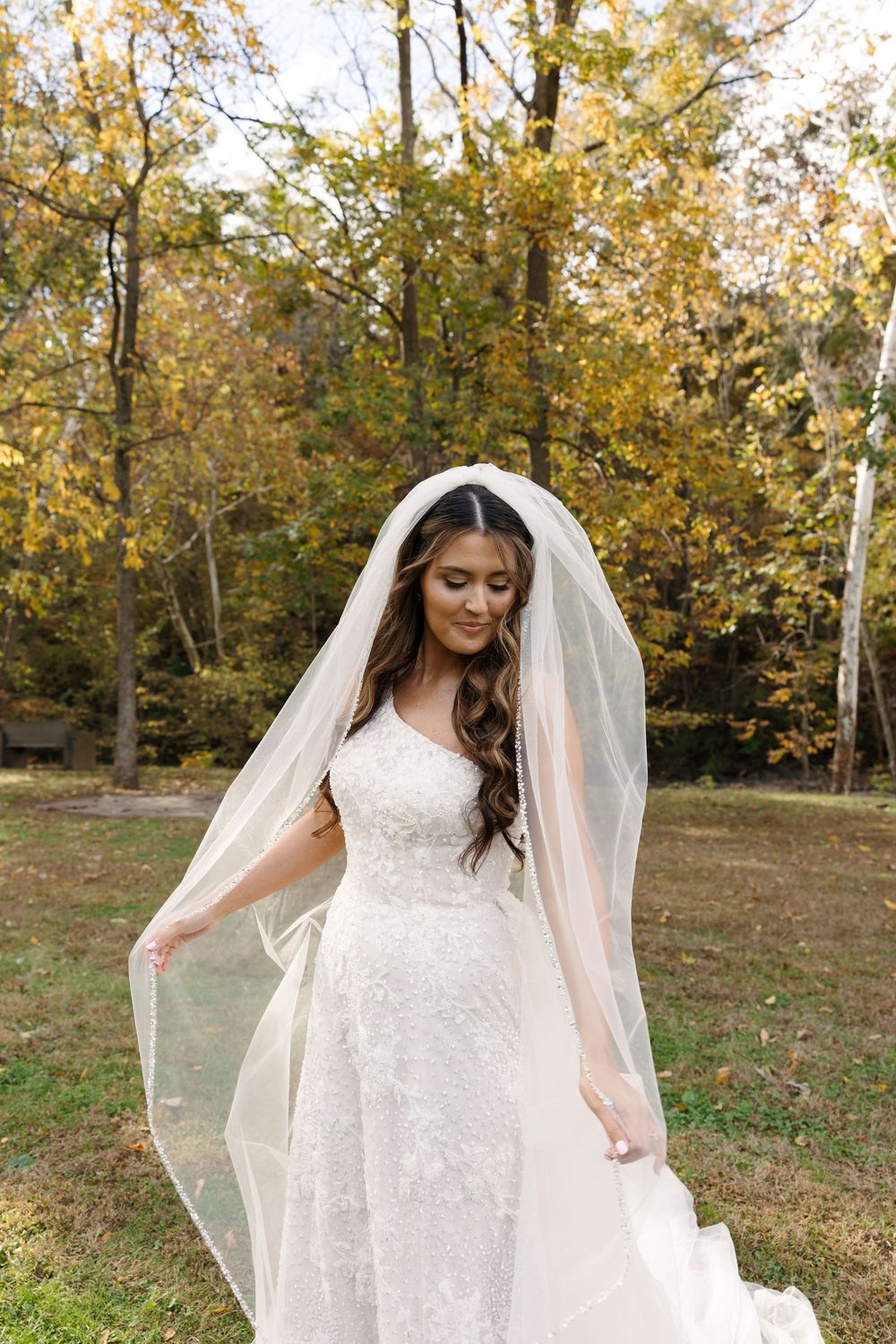 A flowing white wedding dress with veil photographed in an autumn outdoor setting.
