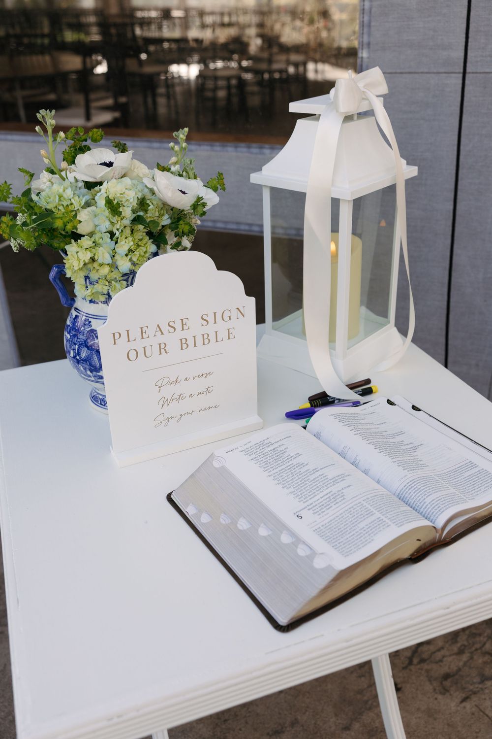 White wedding guest book display with open Bibles and decorative lanterns on a table with blue floral accents.