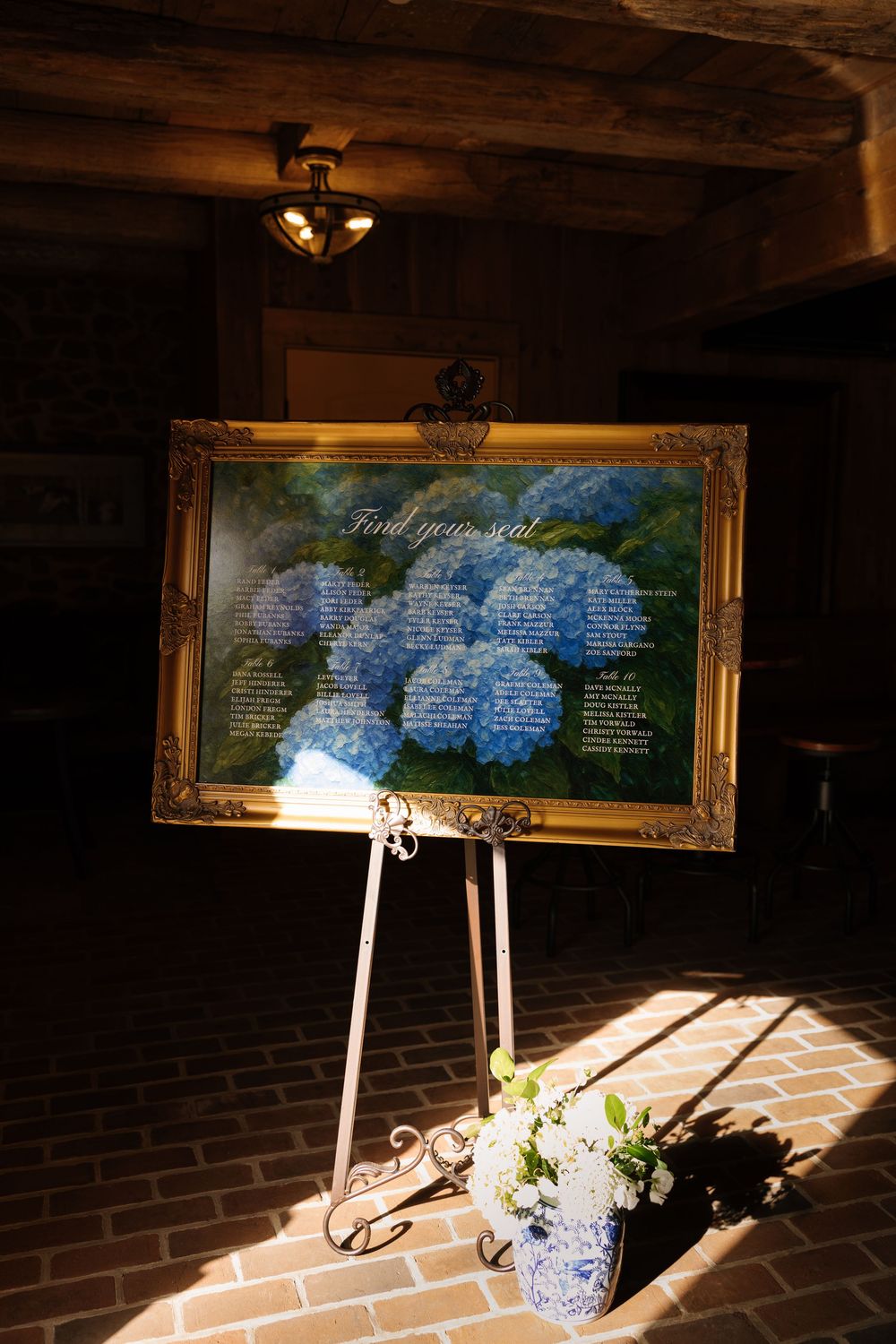 Framed seating charts displayed on elegant stands with blue and white decor in natural sunlight.