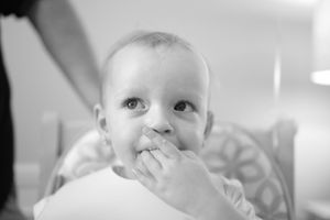Black and white close up photo of a small baby with hand near mouth showing a joyful expression.