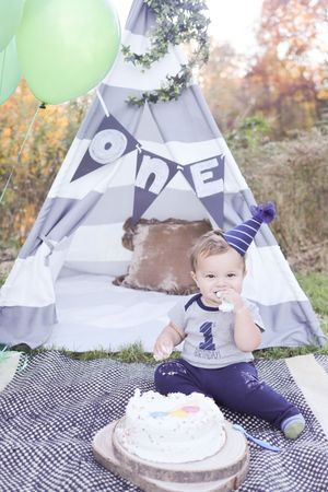 Birthday cake smash photo session outdoors with white teepee tent, checkered blanket and mint green balloons.
