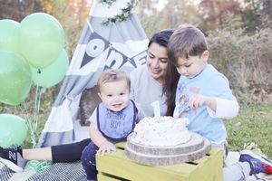 Family enjoys outdoor picnic celebration with cake and green balloons next to gray teepee tent.