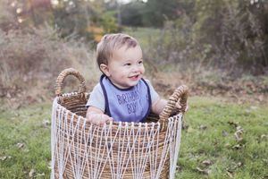 Happy baby sitting in wicker basket during outdoor autumn photoshoot.
