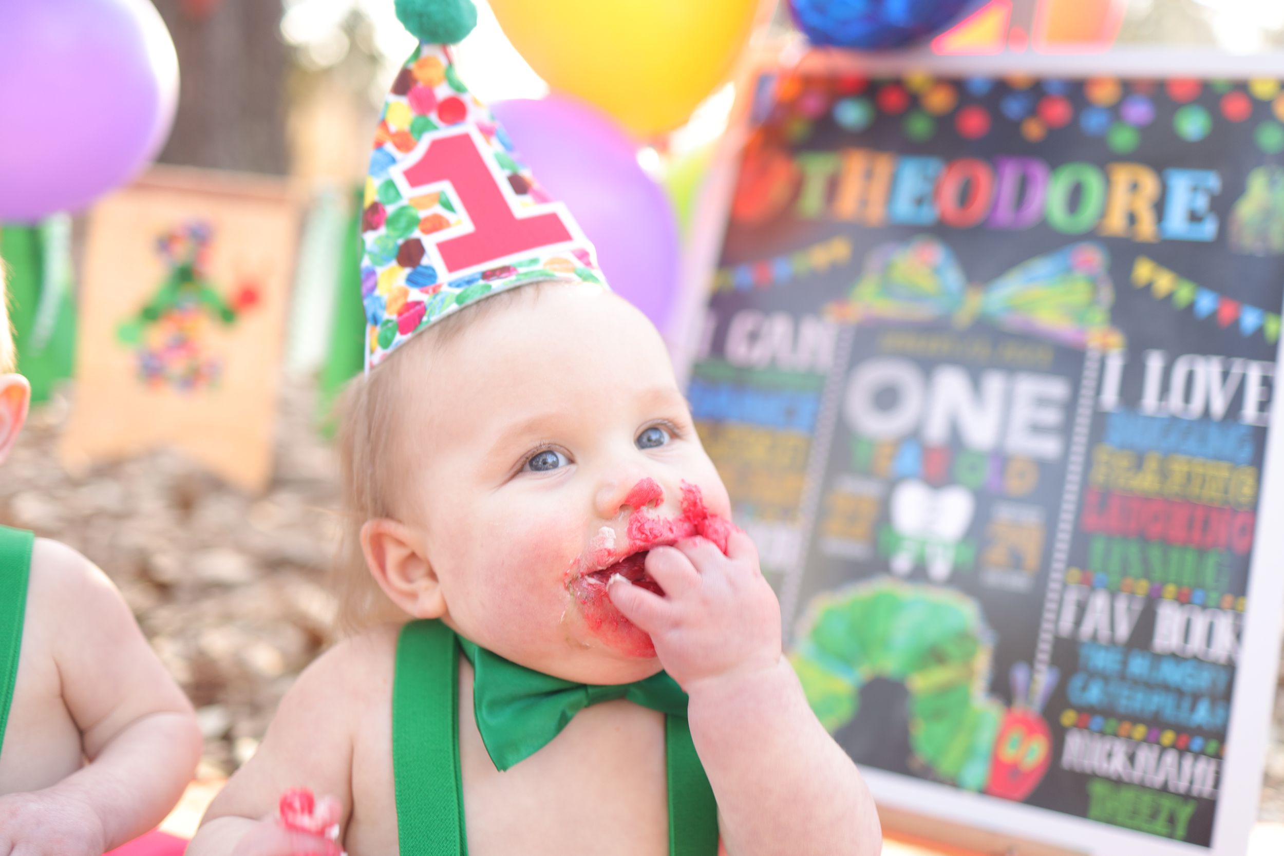 Colorful first birthday party celebration with festive balloons and chalkboard sign in the background.