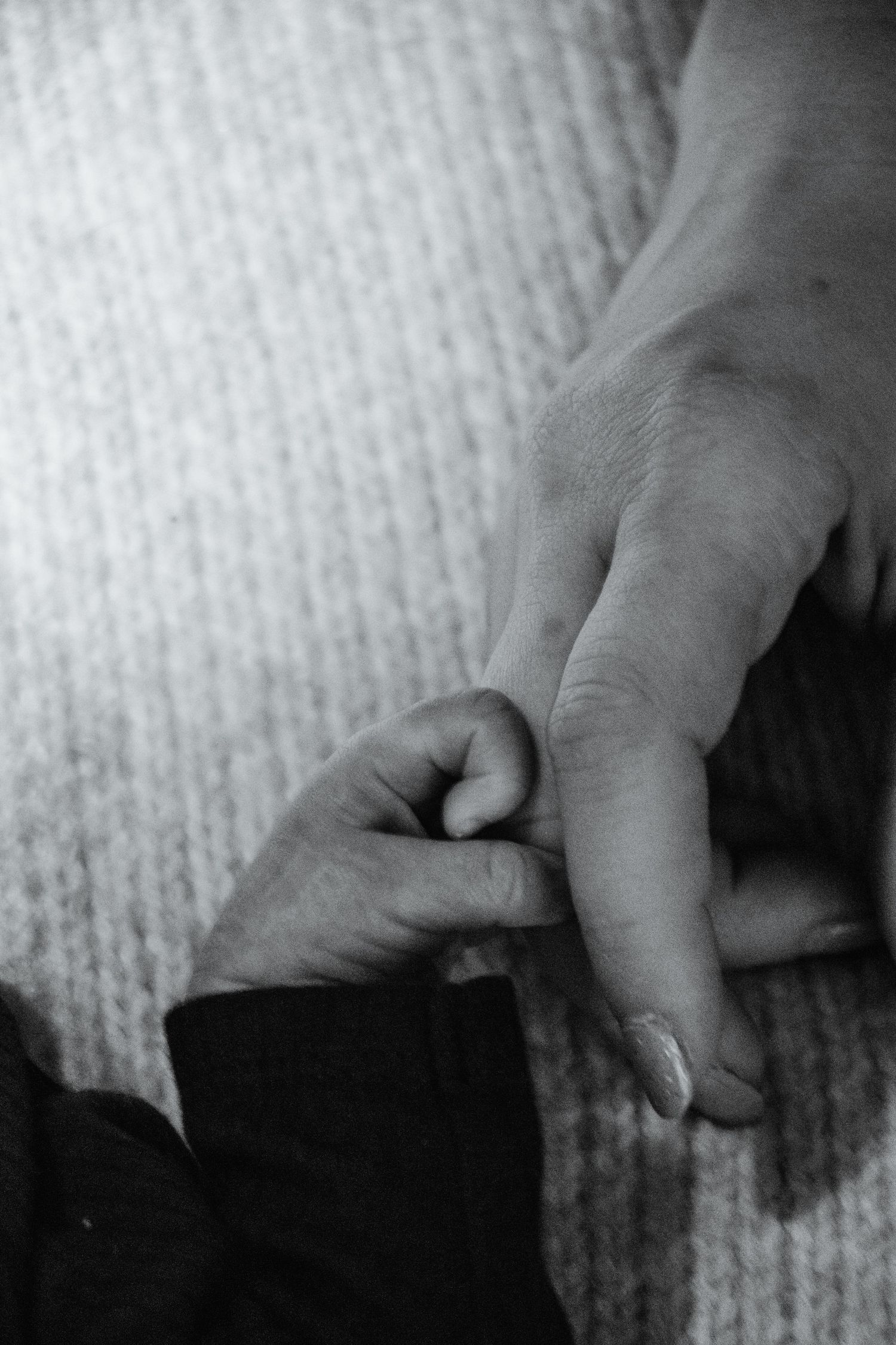 Black & white close-up of a newborn's tiny hand grasping an adult's finger, symbolizing connection and love.