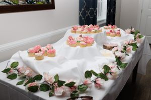 Beautiful display of pink cupcakes decorated with flowers on a white tablecloth with rose petals.