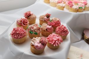 Elegant cupcakes topped with pink floral decorations arranged on a white serving platter.