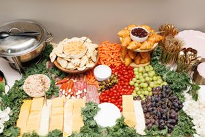 Gourmet appetizer spread featuring cheese, fruits, vegetables and dips arranged on green garnish.