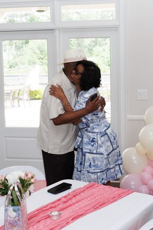 Guests embracing at a celebration with pink balloons and decor in the background.