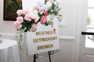 A decorative sign for Heather's Retirement Brunch with pink floral arrangements.