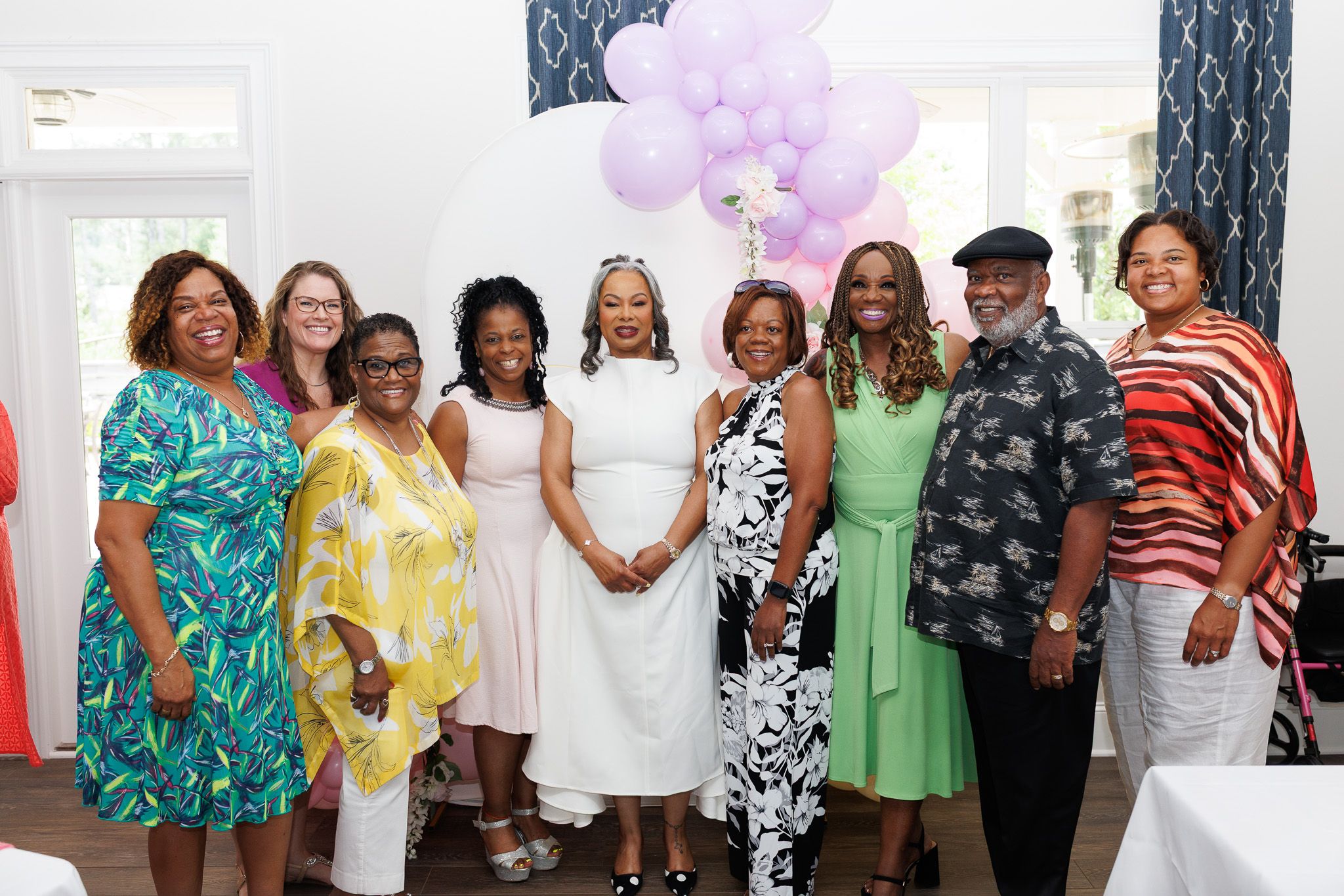 Group celebrating at a party wearing colorful dresses and outfits with balloons in background.