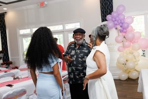 People mingling and socializing at an indoor party with purple balloons and white decor.