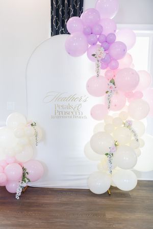 Elegant balloon arch with pink, purple and white balloons against light gray wall.