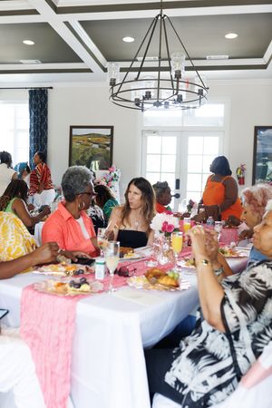 Guests seated at tables decorated with pink runners under a large circular chandelier.