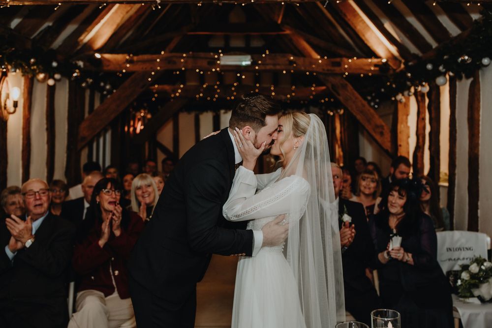 A couple shares a romantic dance in a rustic barn venue with warm lighting and wedding decorations.