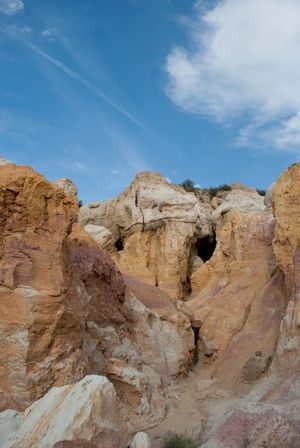 Rugged sandstone cliffs with pink and tan striations form a natural cave opening against a bright blue sky.
