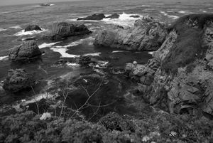 Black and white coastal landscape with rugged cliffs and crashing waves along a rocky Northern California shoreline.