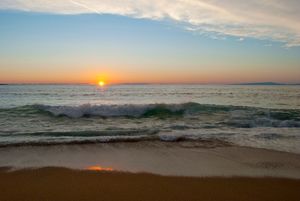 Sunset over the ocean with rolling waves crashing on sandy beach during golden hour.