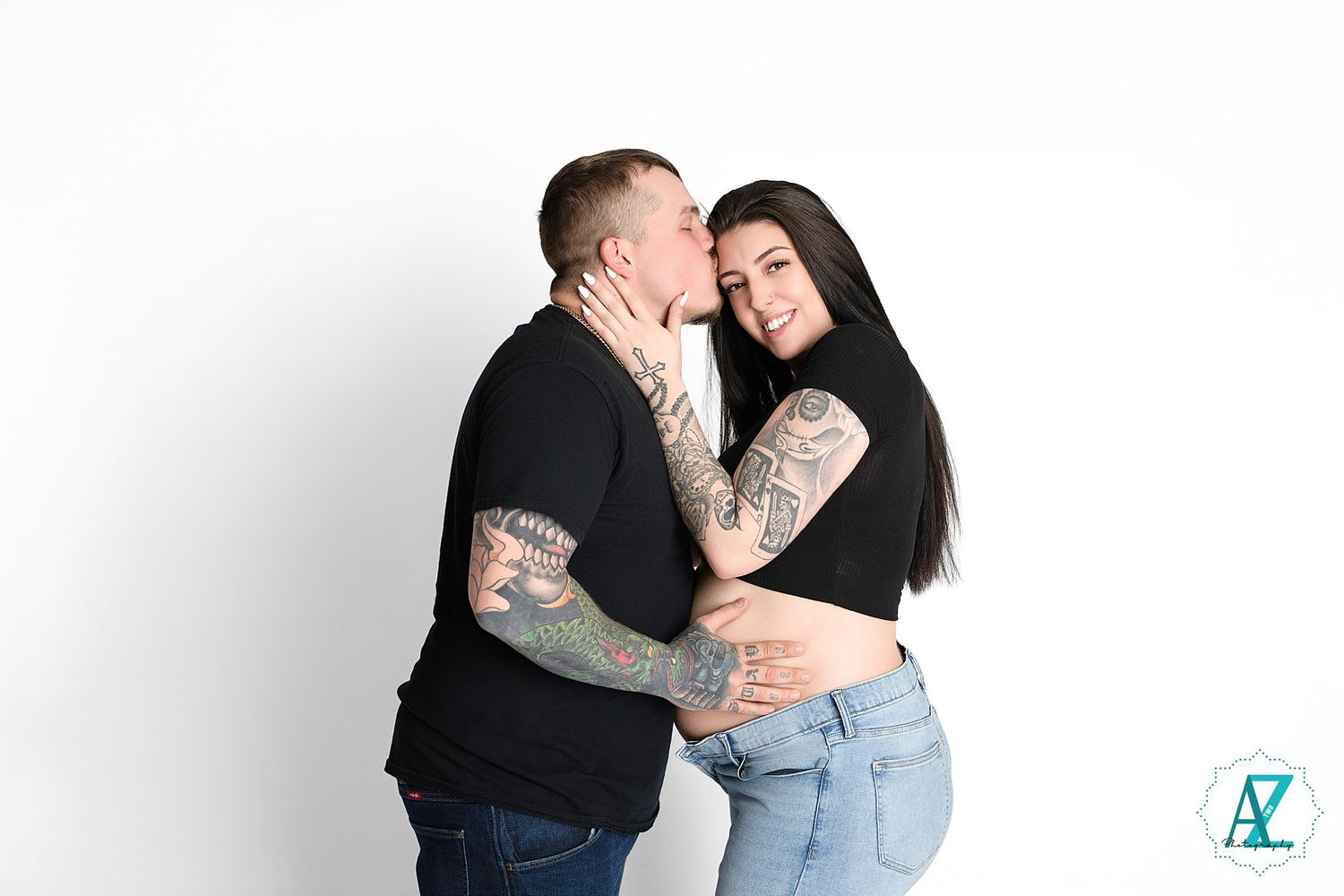 Two tattooed individuals share an intimate embrace against a white studio backdrop.