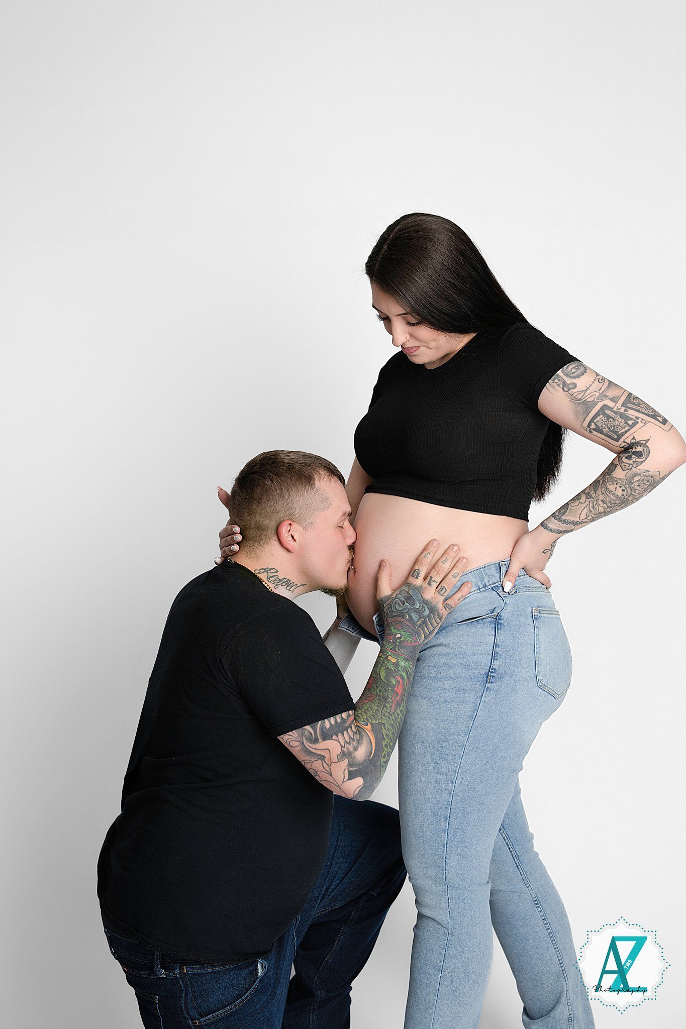Expecting couple in black tops share intimate moment against white backdrop as they await their baby's arrival.
