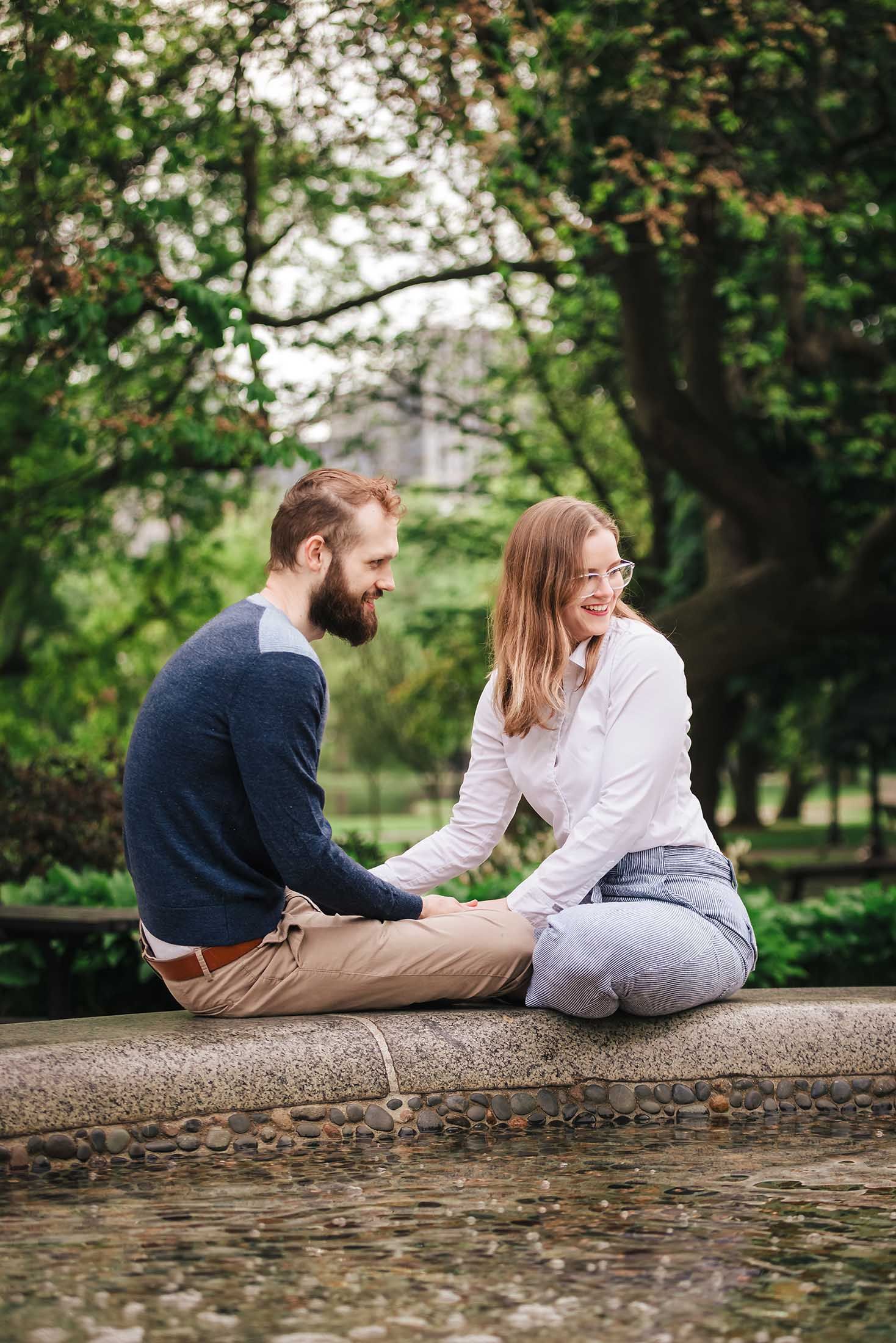 Joyful moment of engaged couple sitting together on the edge of the George Robert White Memorial Fountain in Boston Public Garden engagement