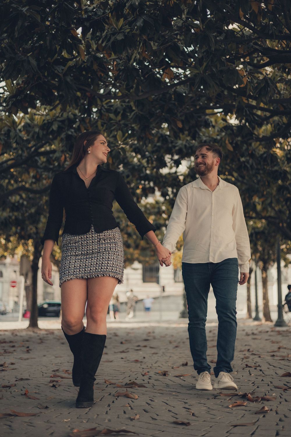 Couple walking through a leaf-covered path holding hands.