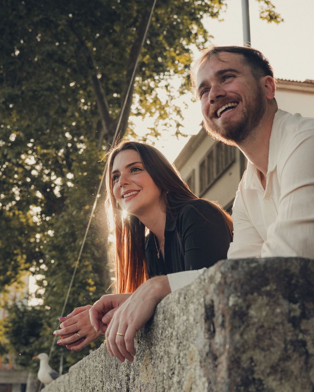 Romantic sunset couple moment along stone wall with warm golden light.