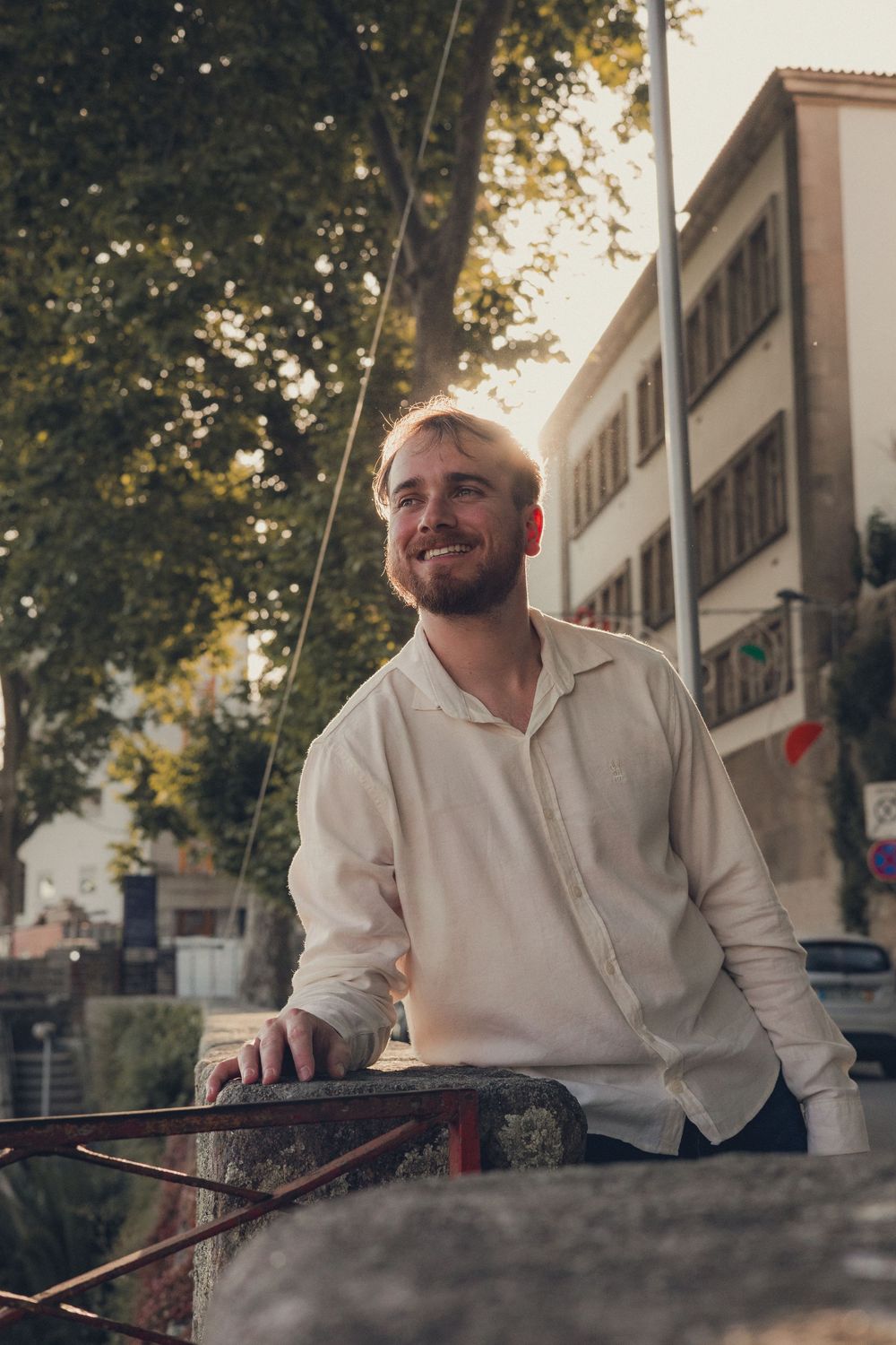 Person in white shirt smiling and leaning against wall during sunset.