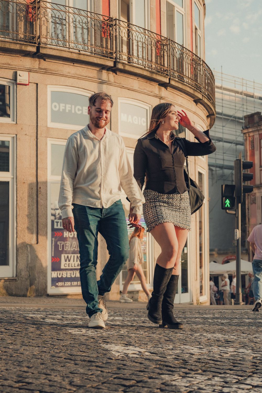 Couple walking on cobblestone street past vintage storefronts.