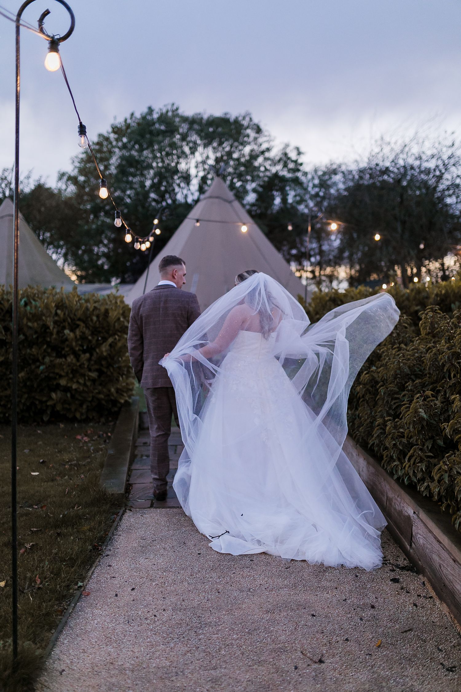 A romantic evening walk along a path with string lights overhead and a flowing white wedding dress. Photographer. Hull. East Yorkshire. Phot