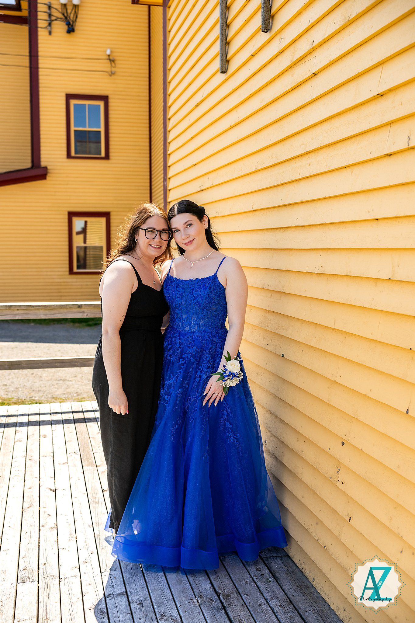 People in formal wear posing for photos against yellow wooden siding of a house on a porch.