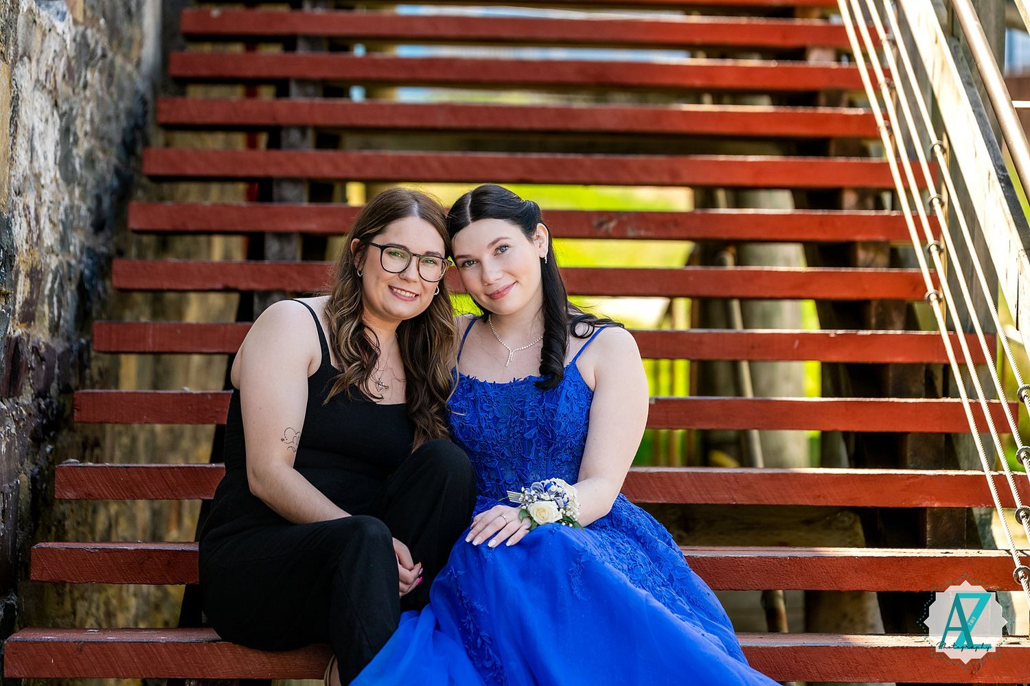 Two people in formal dresses sitting together on outdoor wooden stairs.