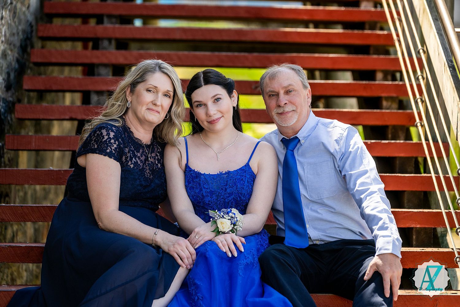 Group in formal attire sitting together on rustic wooden stairs with navy and royal blue dresses.