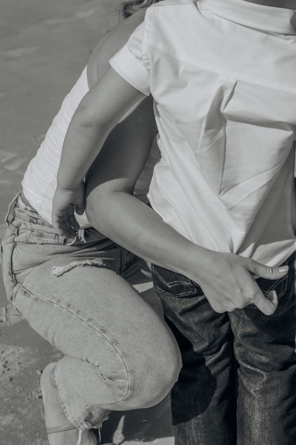 Black and white close-up of woman in white top and distressed jeans crouching down.