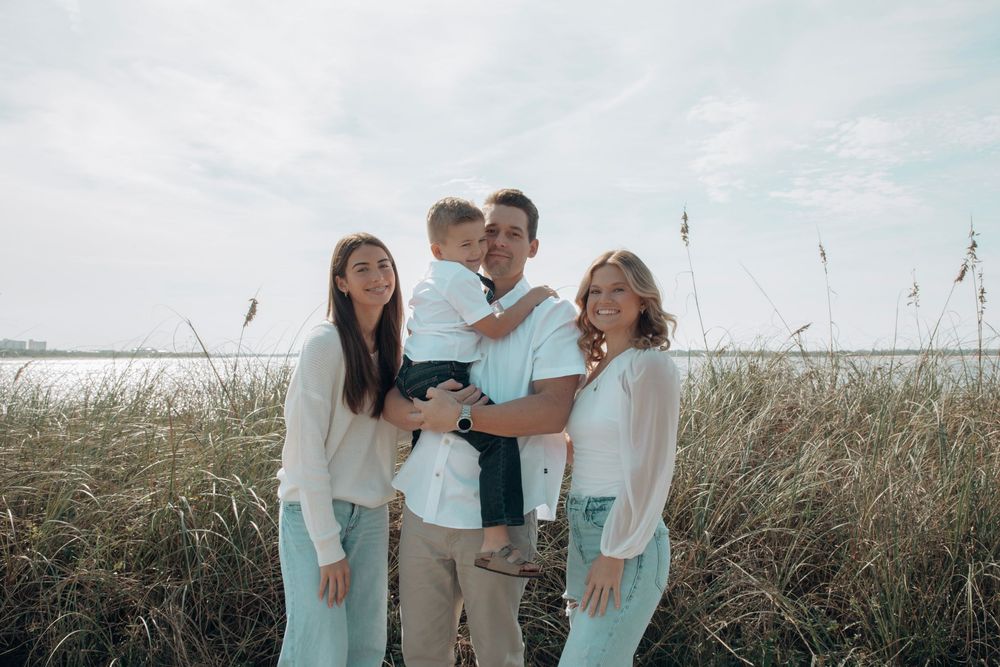 Happy family of four posing together in tall beach grass near the water.