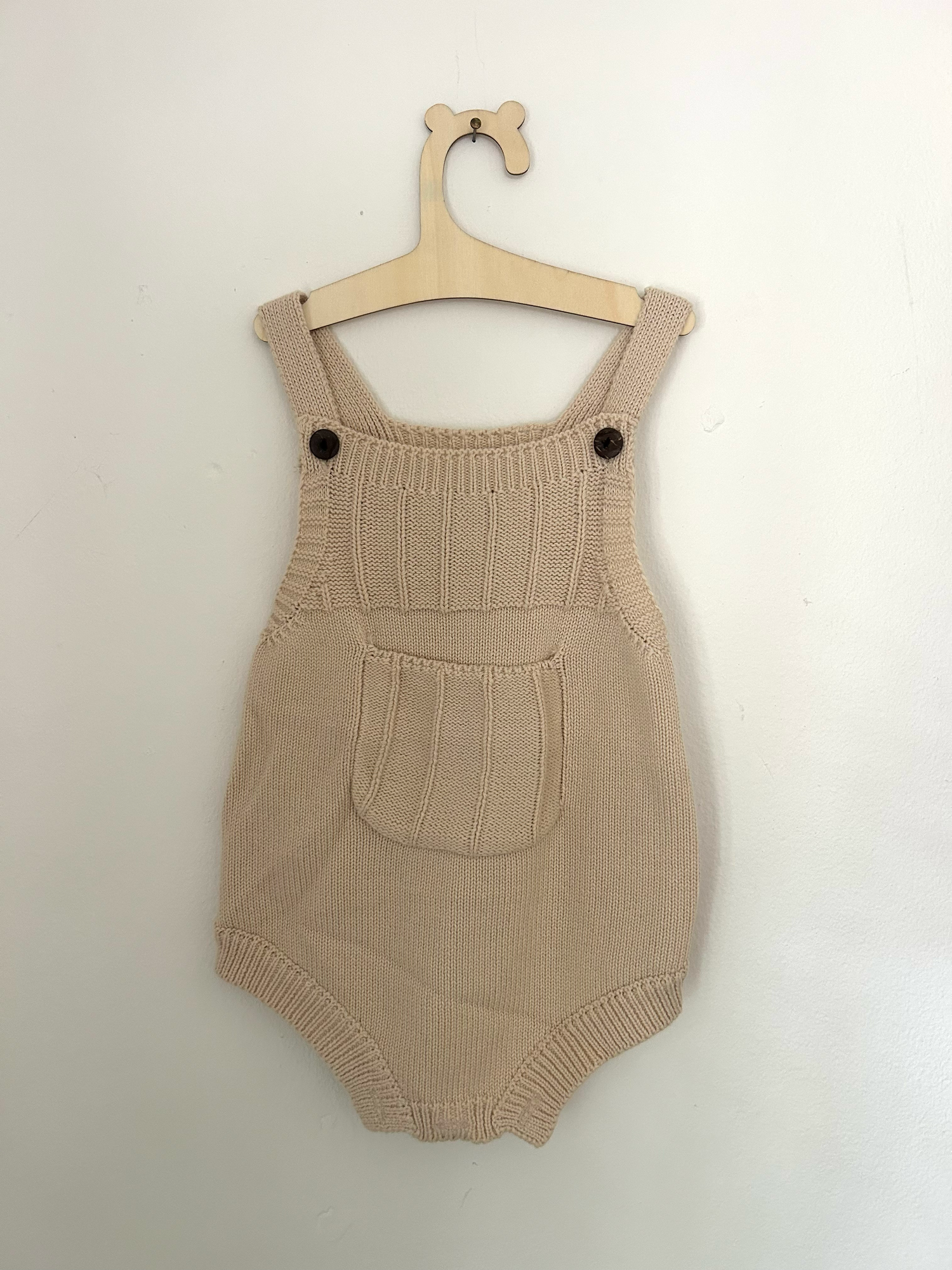 White knit baby romper with 'ONE' text and small bow detail in pink embroidery against hanging clothing background.