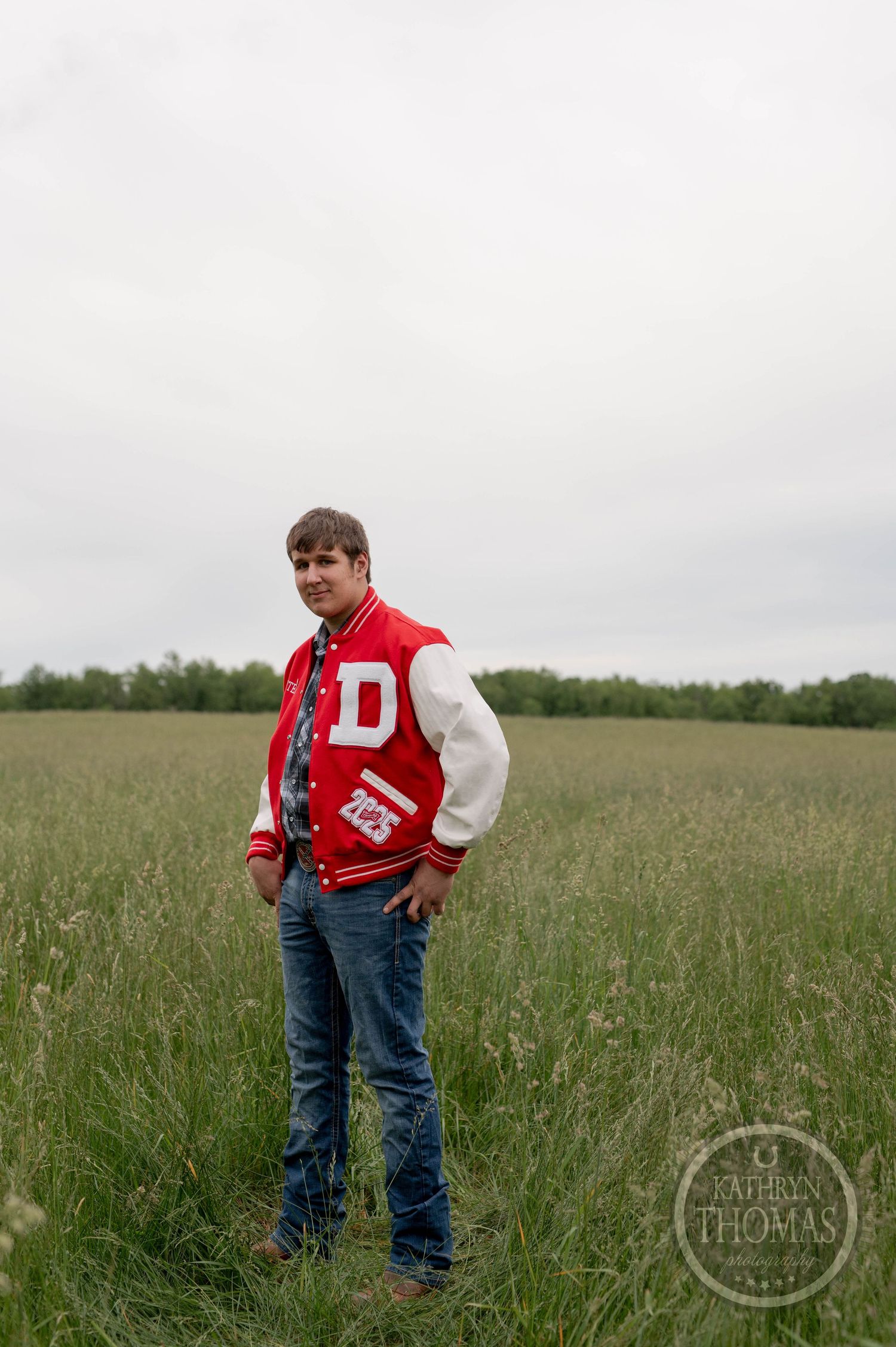 A letterman jacket wearer stands in a grassy field on an overcast day.