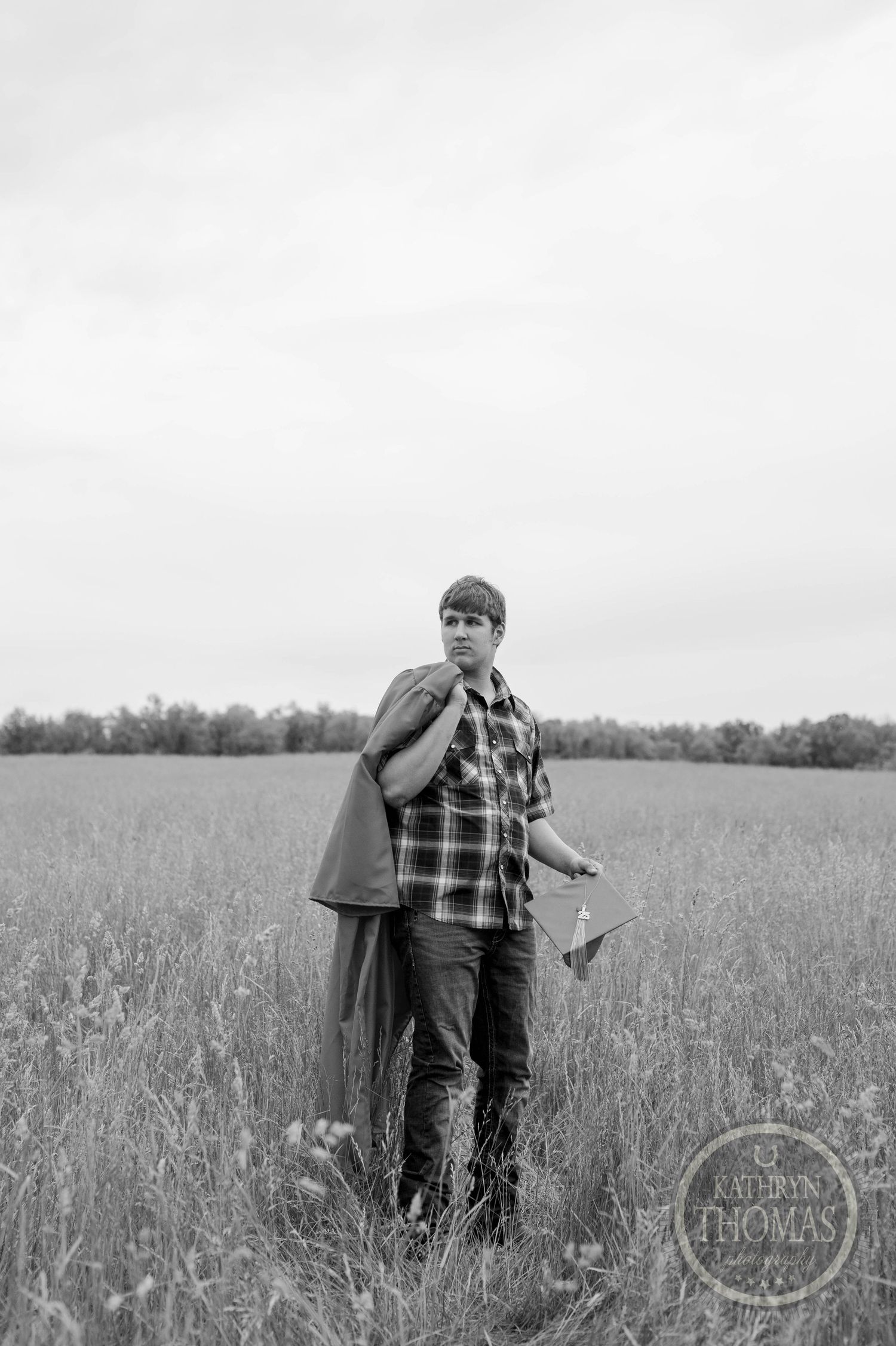 A figure stands contemplatively in a tall grass field on an overcast day against a moody sky.
