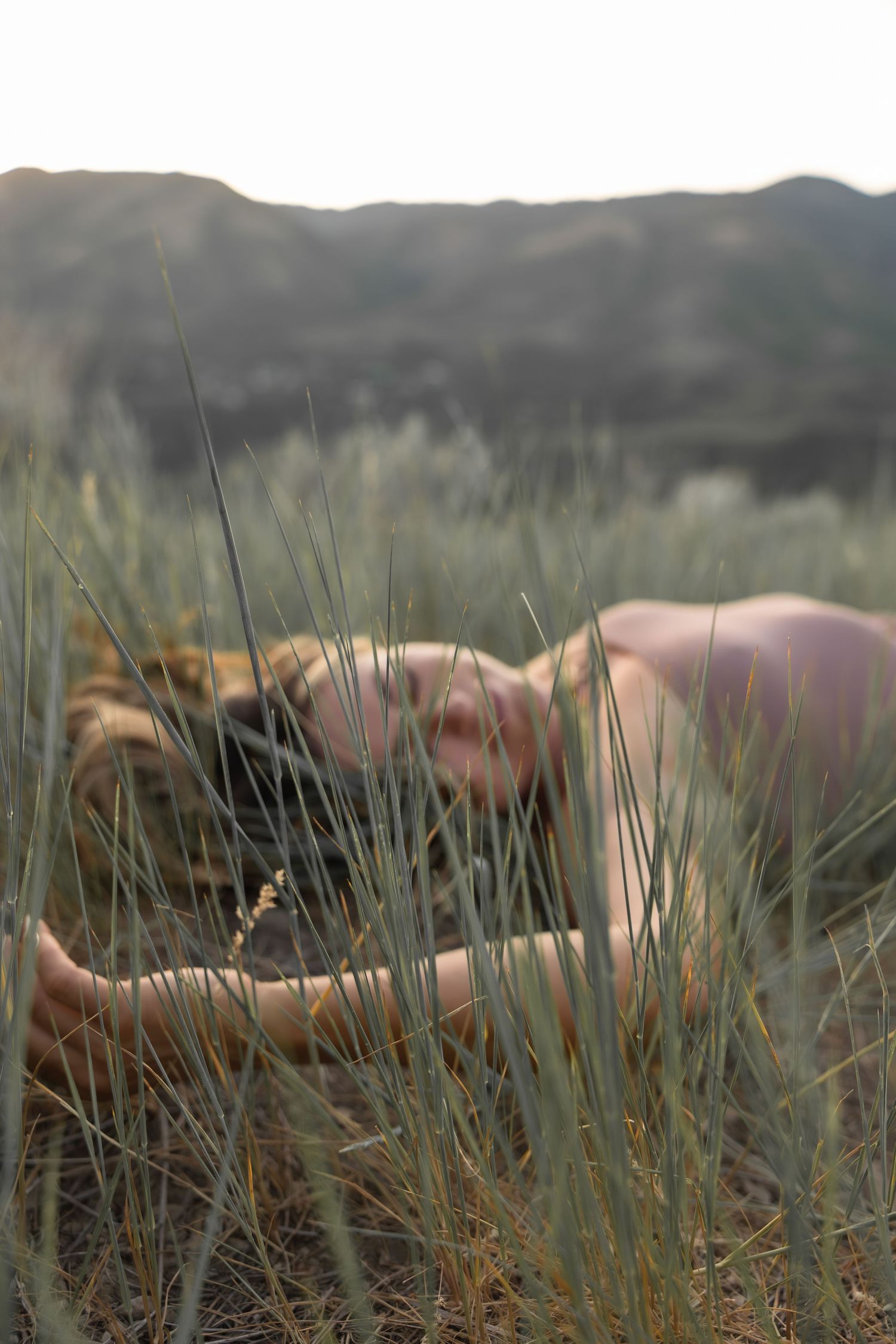 A woman lying in tall grass with mountains in the background during golden hour lighting.