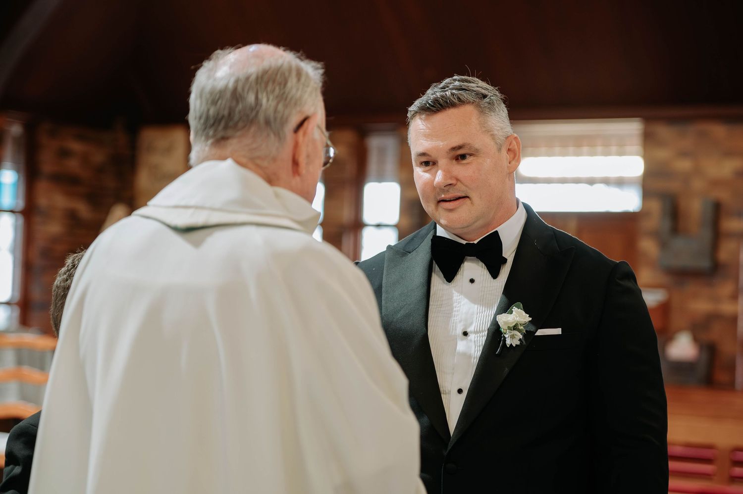 Two people converse during a formal event in a rustic setting with brick walls and wooden accents.