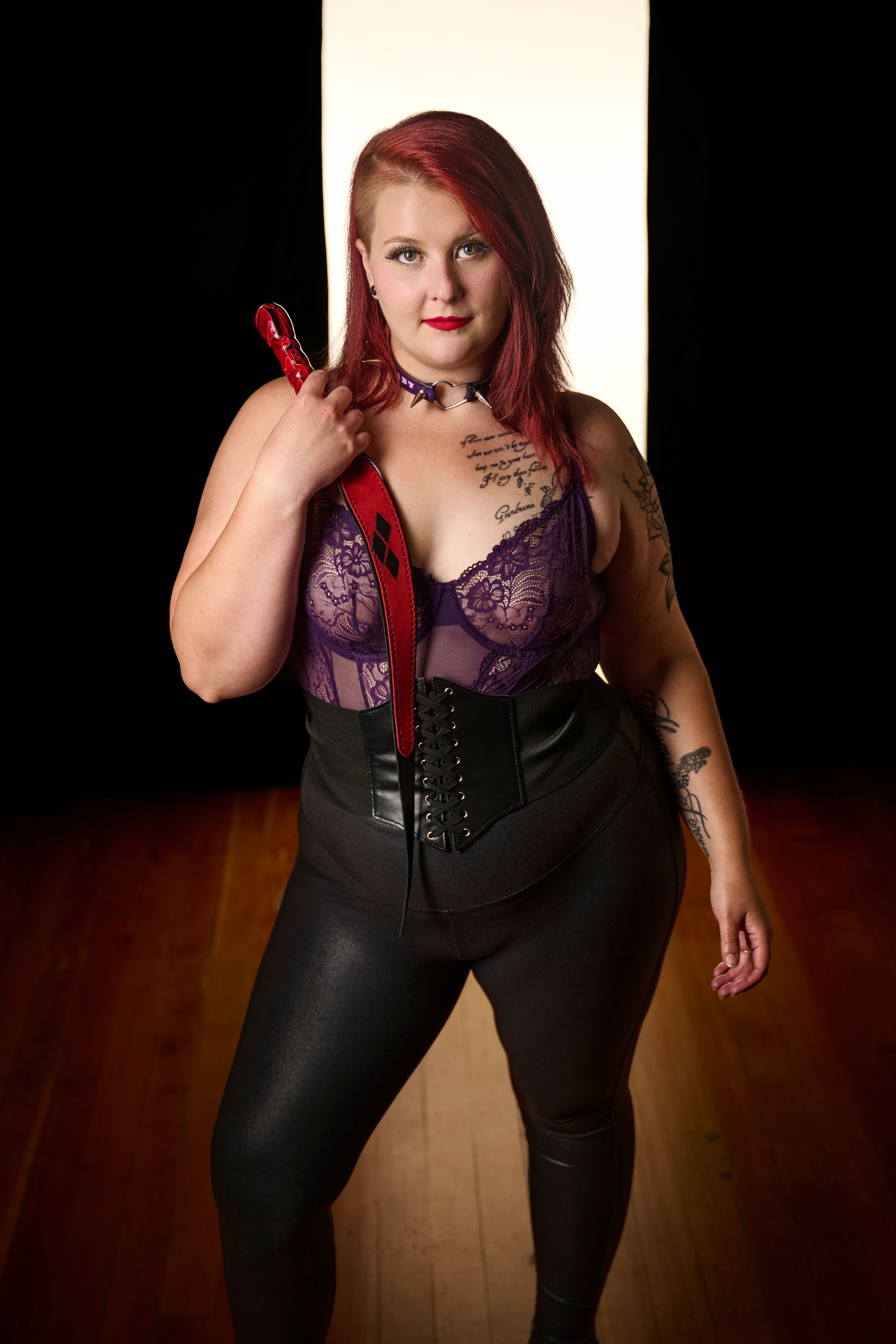 A person wearing a purple lingerie top and black corset poses confidently against a light background.