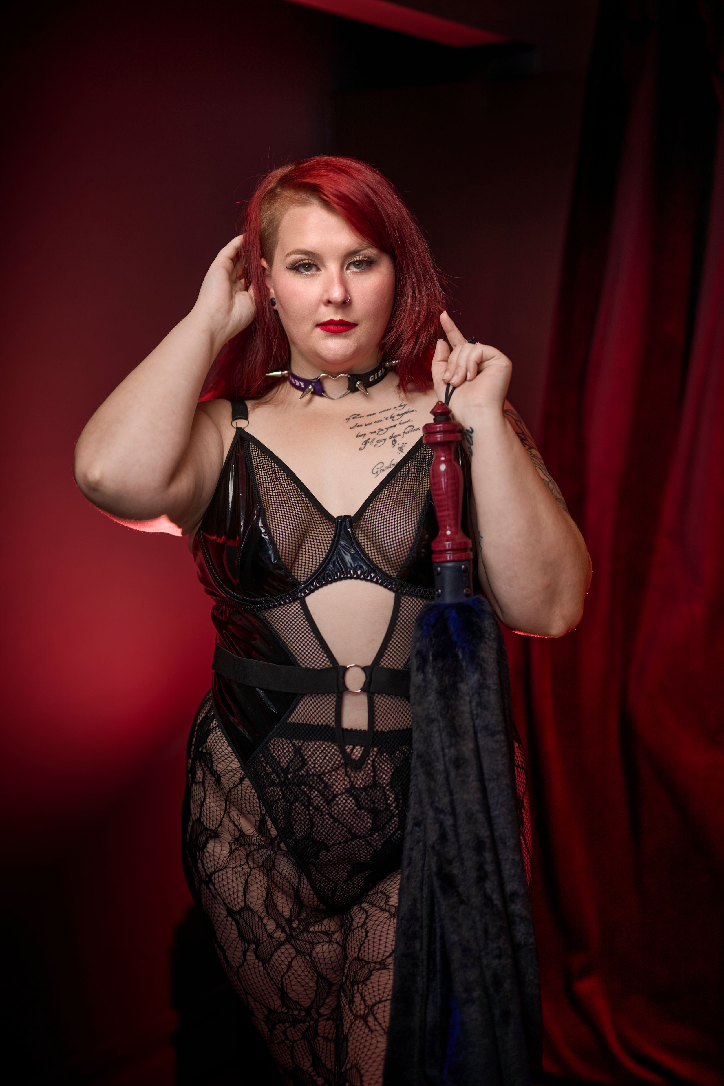 Portrait of someone in black lace lingerie against a red curtain backdrop.
