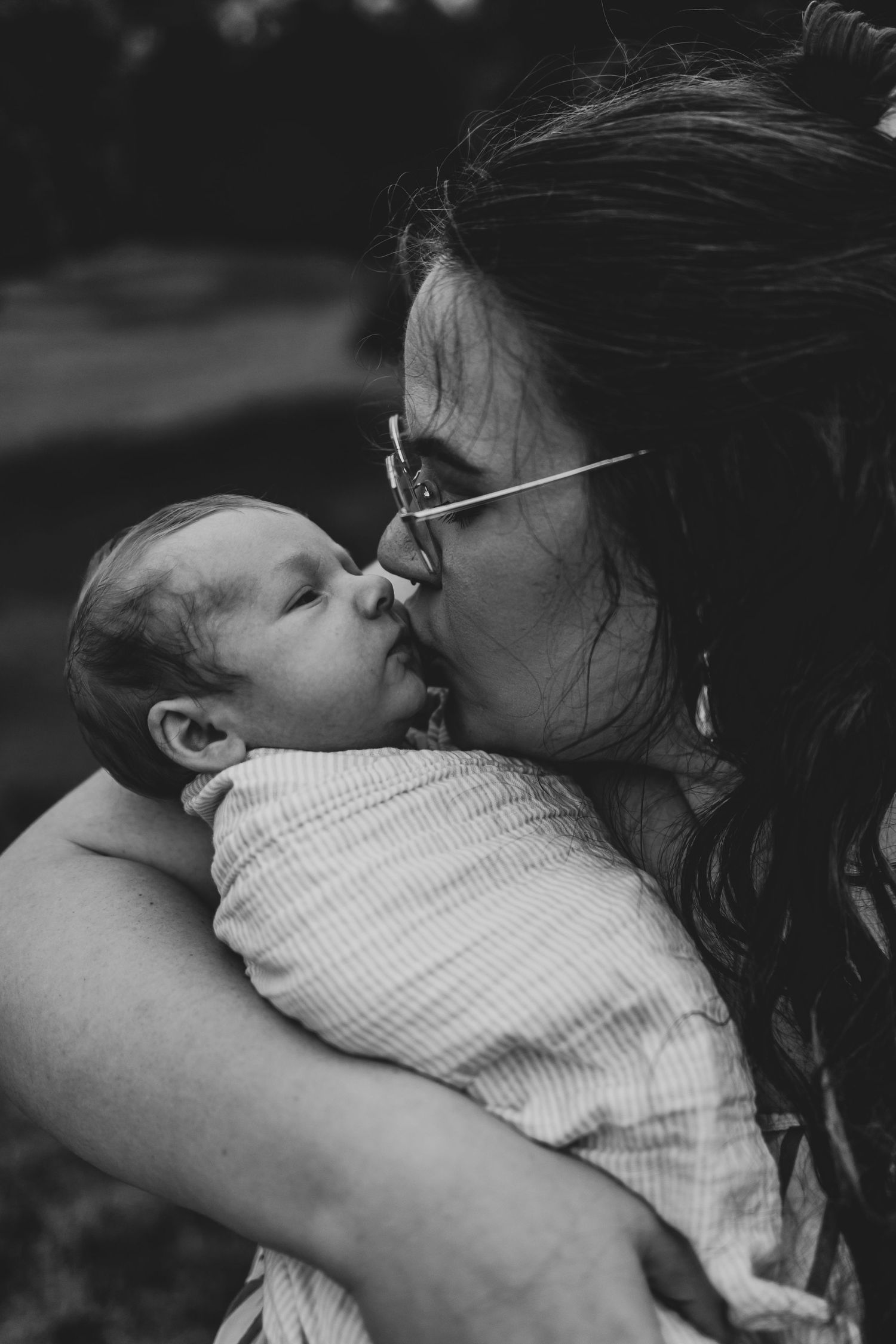 Mother kissing her newborn son on the cheek at their family session, newborn session