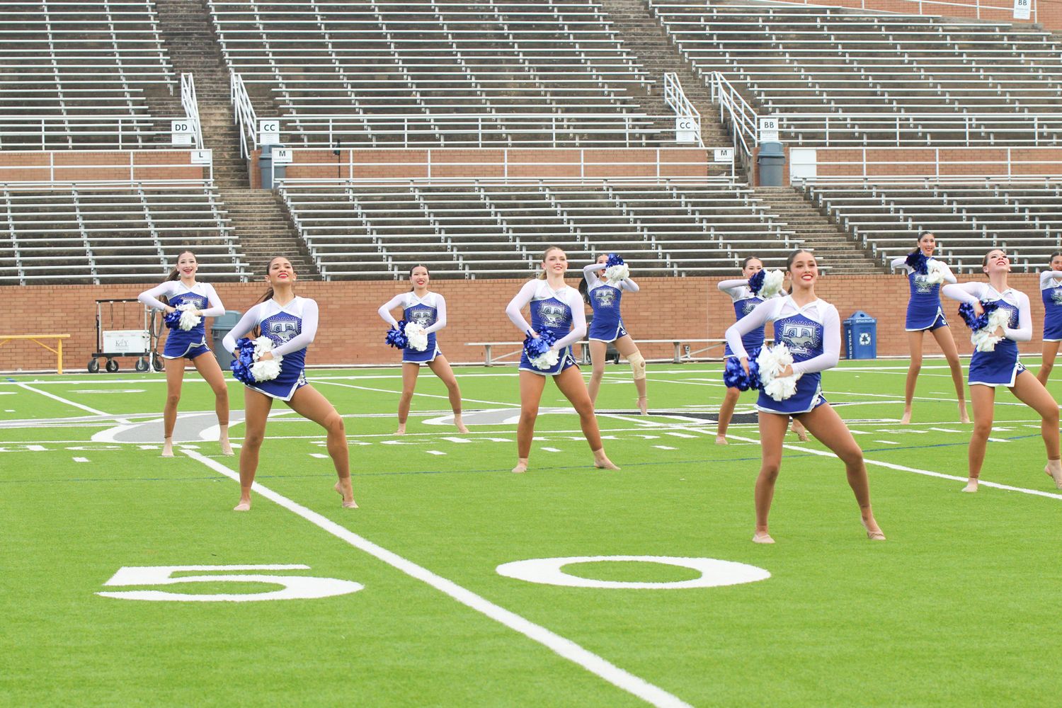 Cheerleaders in blue and white uniforms perform synchronized dance routine on football field during practice.